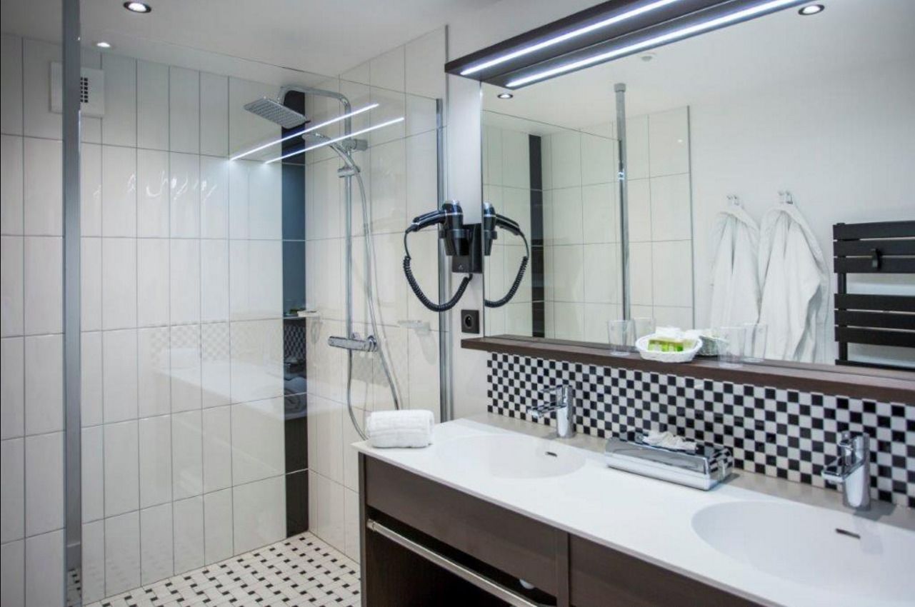 Un baño moderno con ducha de vidrio, un lavamanos blanco y un tabique a cuadros, y un espejo grande.
