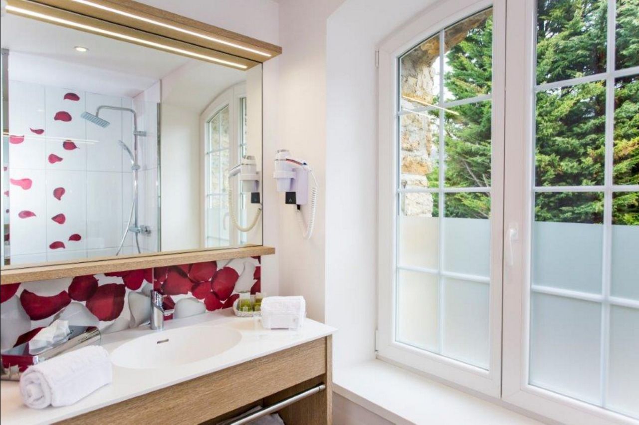 A bathroom with a large mirror, white sink, and a window with frosted glass.