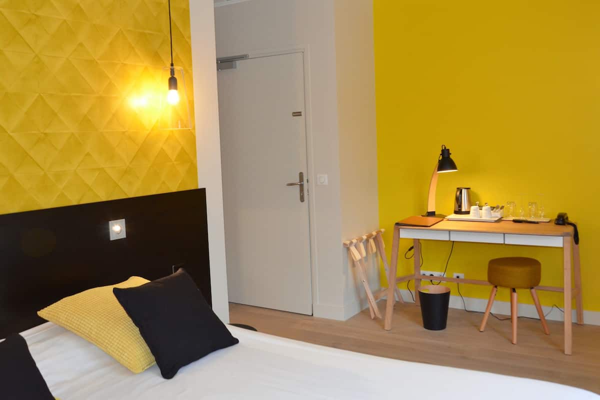 Ein Zimmer mit einem Bett, einem Schreibtisch und einem Stuhl. Im Hintergrund ist eine Tür zu sehen.