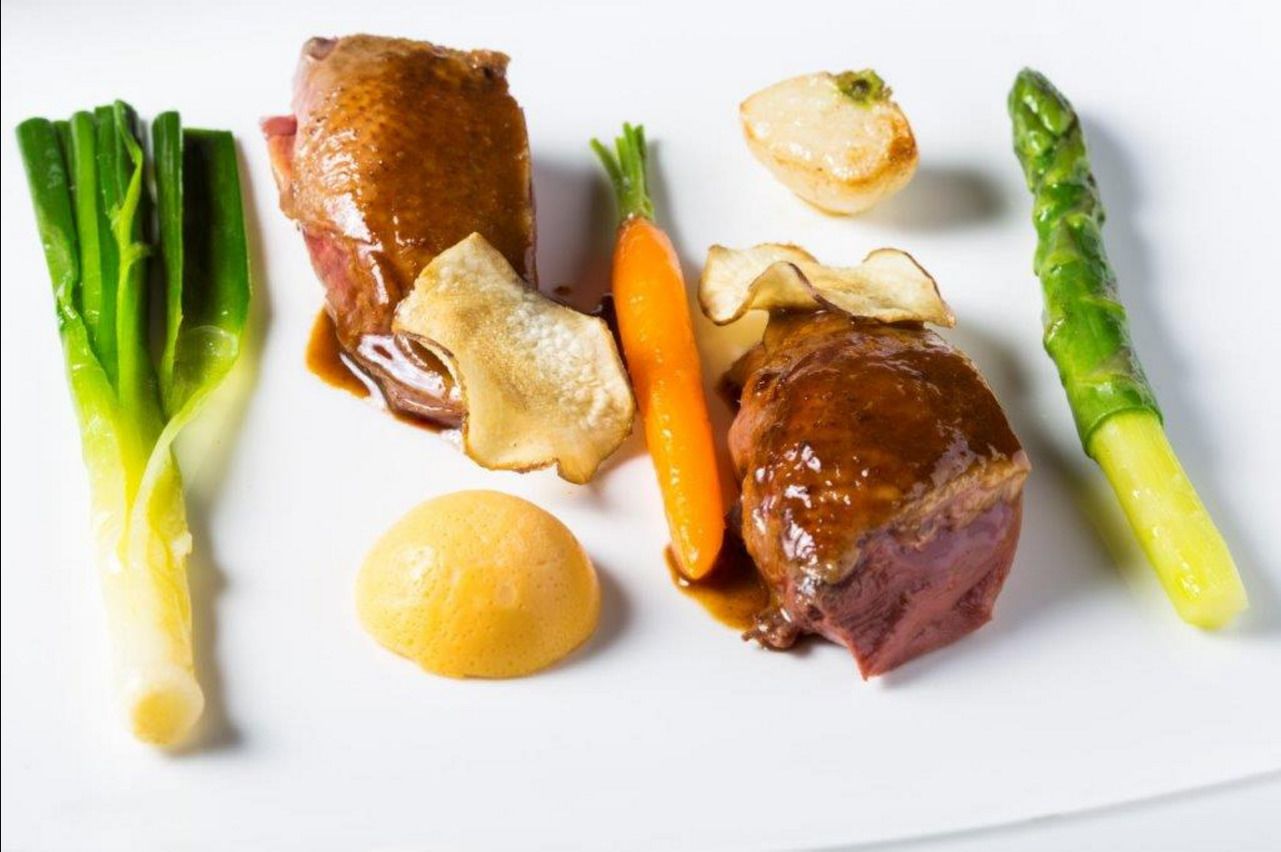 A plate with a piece of meat, vegetables, and a small round item.