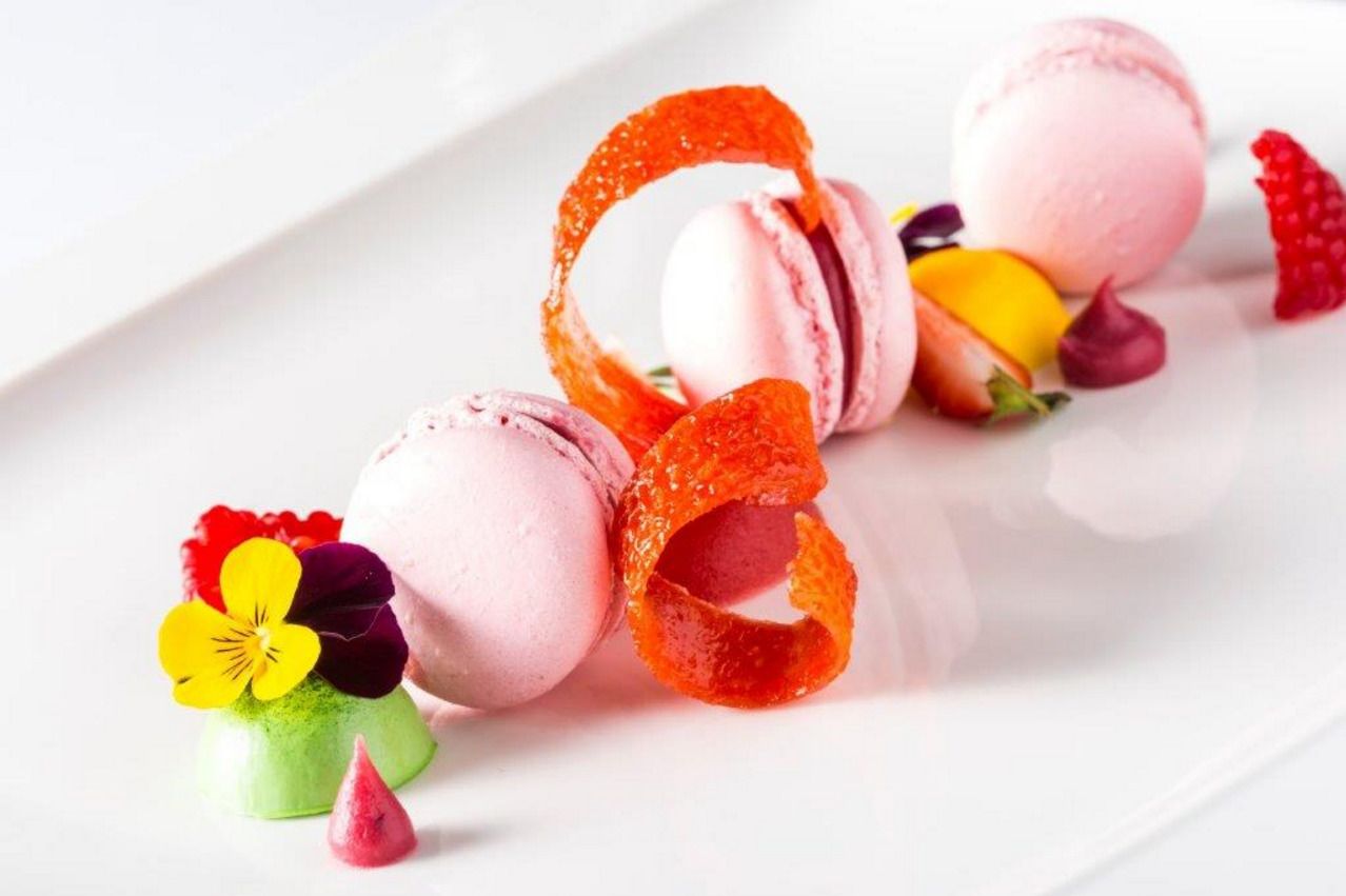 Une assiette à dessert décorée de macarons, de fleurs colorées et d’une base verte.