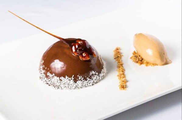 Un postre con una capa caramelizada, una cucharada de crema y espolvoreado de migas sobre un plato blanco.