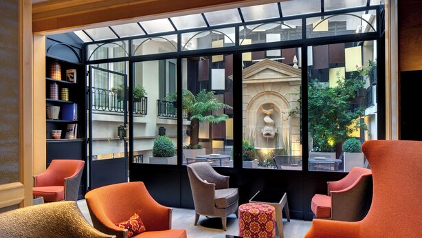 A modern lounge with comfortable seating, a glass partition, and a view of the cityscape. - Hotel Rochester Champs Elysées (Paris)