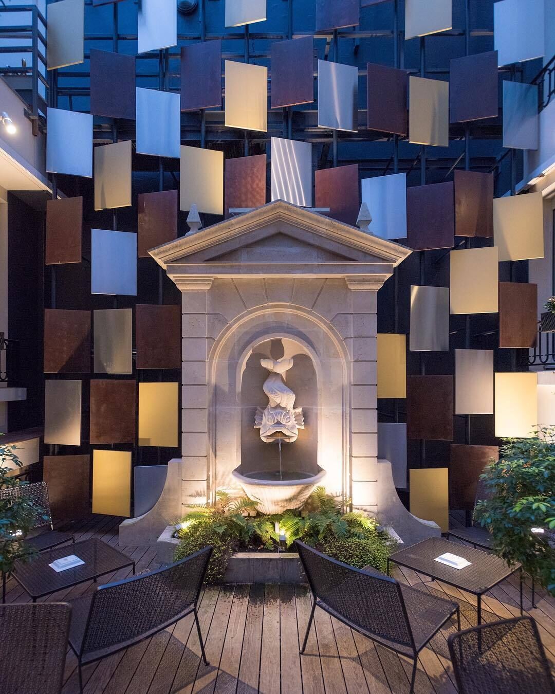 Une cour avec une fontaine, un espace aménagé pour s’asseoir et la façade d’un bâtiment moderne ornée de motifs géométriques.