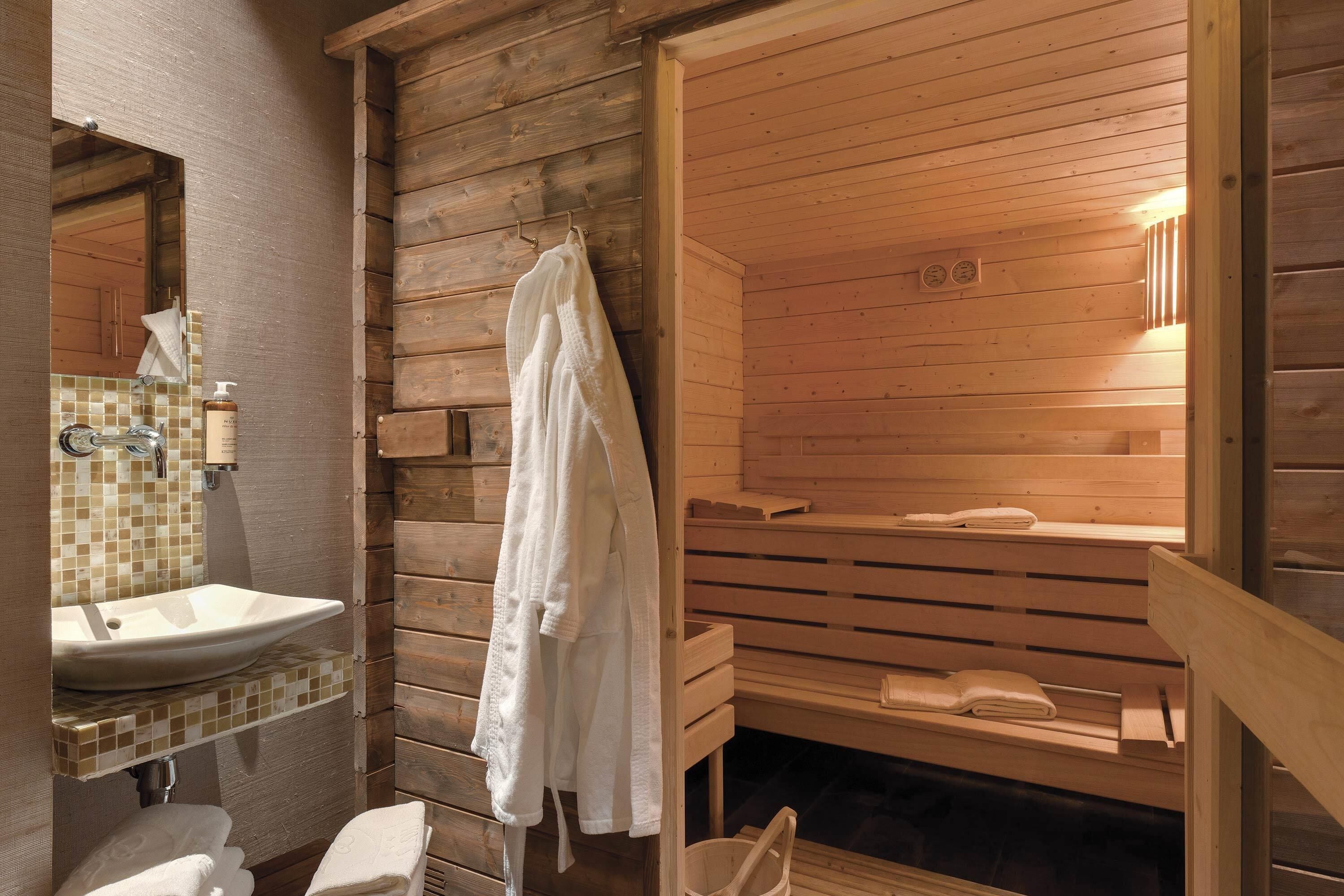 A wooden cabin-style bathroom with a sink, mirror, towel rack, and wooden benches.
