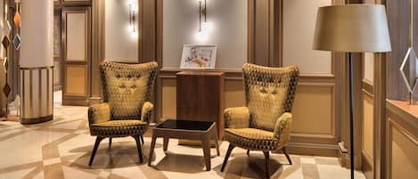 A lobby with two upholstered armchairs, a small table, and a wall-mounted light fixture.