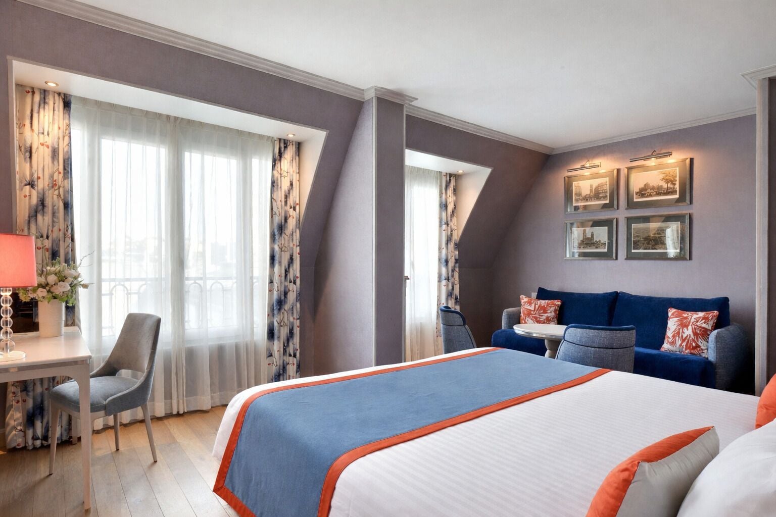 A hotel room with a bed, a desk, a chair, a sofa, and a dining table.