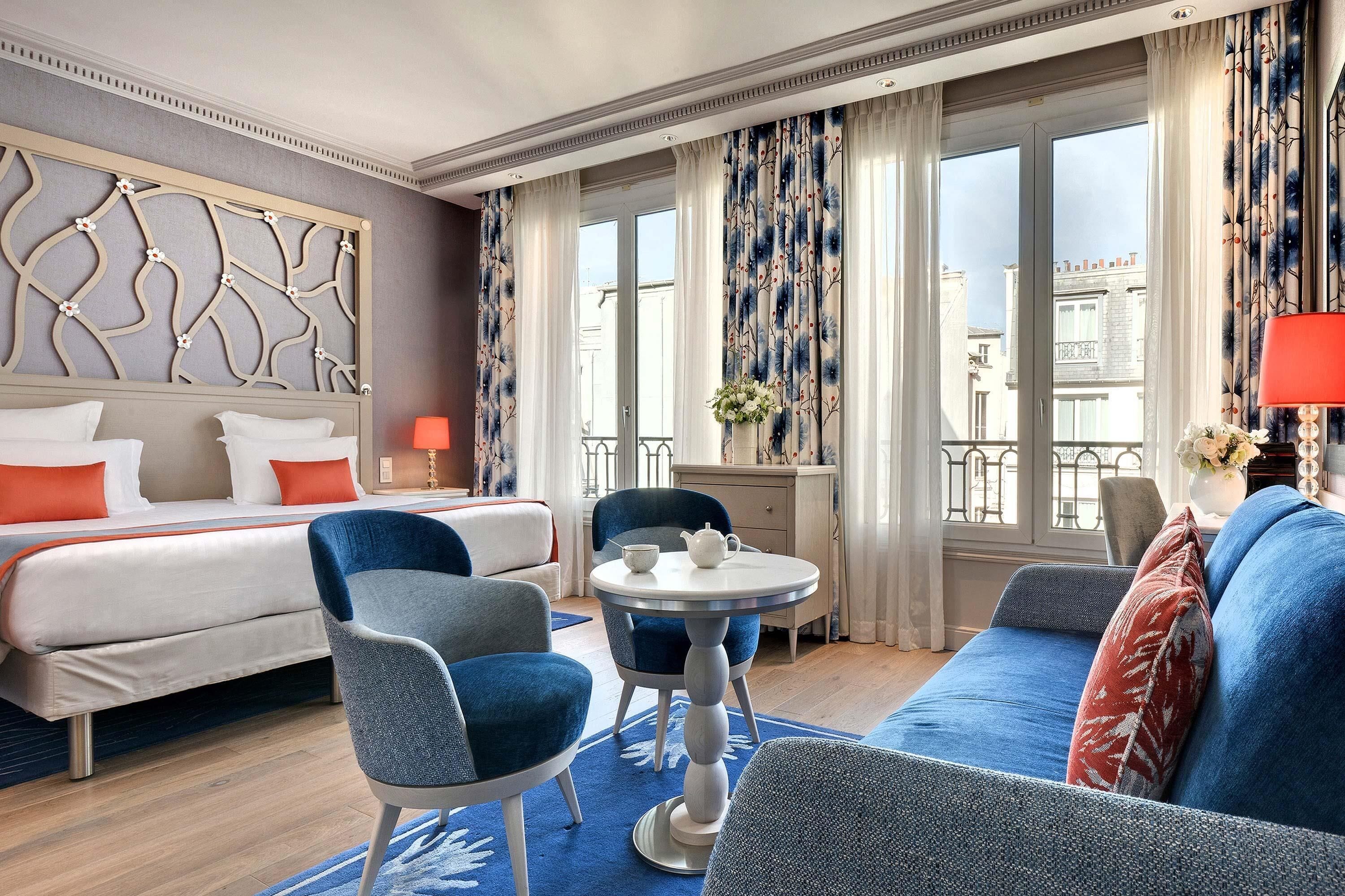 A hotel room with a bed, two armchairs, a small table with a teapot, and a sofa.