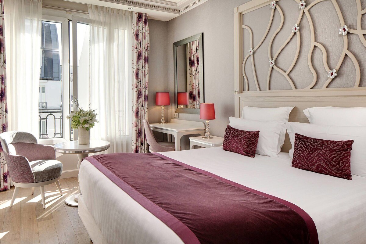 Habitación de hotel con una cama grande, un escritorio, una silla y vista a la ciudad.