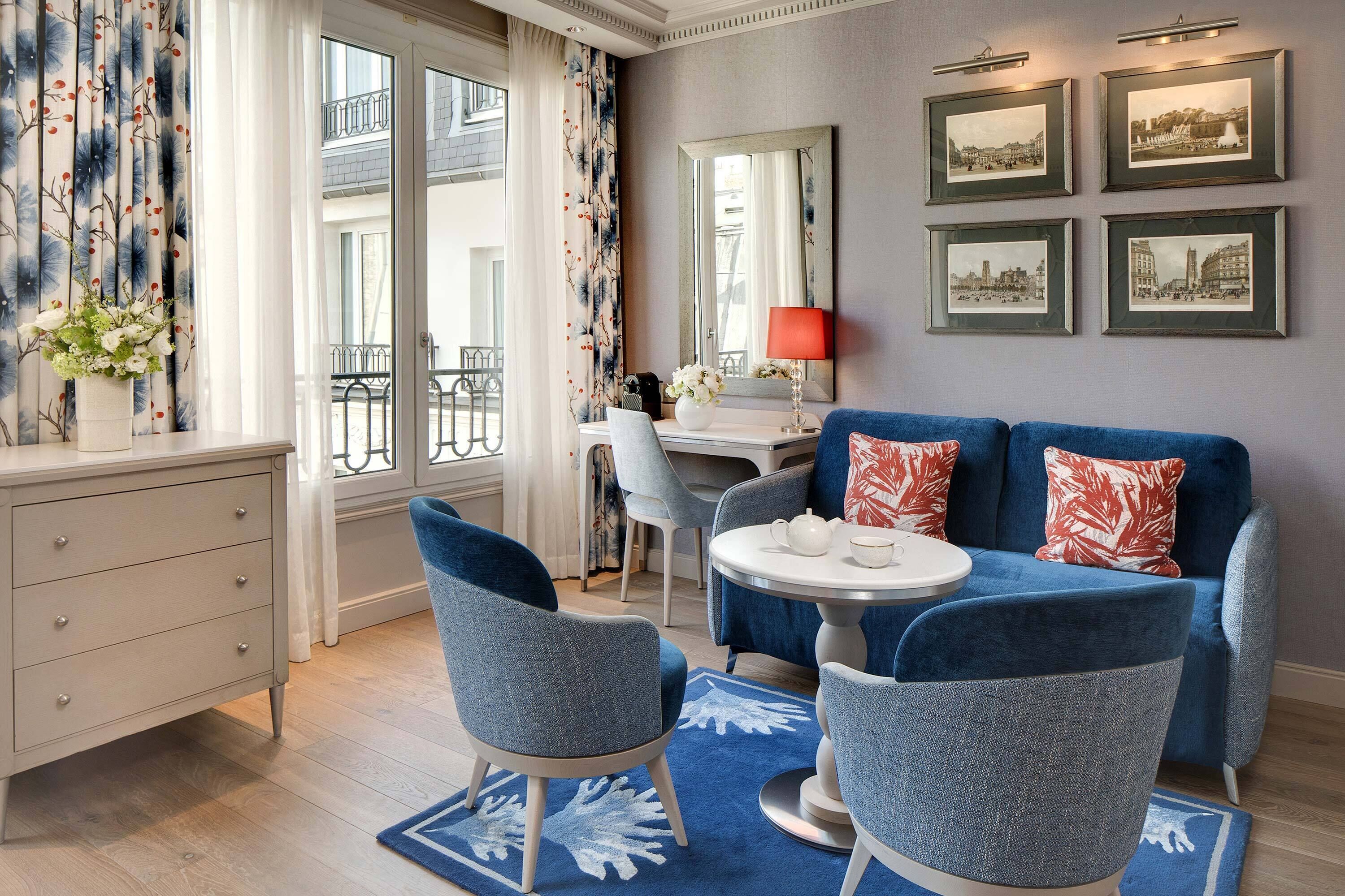A modern room with a blue sofa, two chairs, a round table, a dresser, and a mirror.