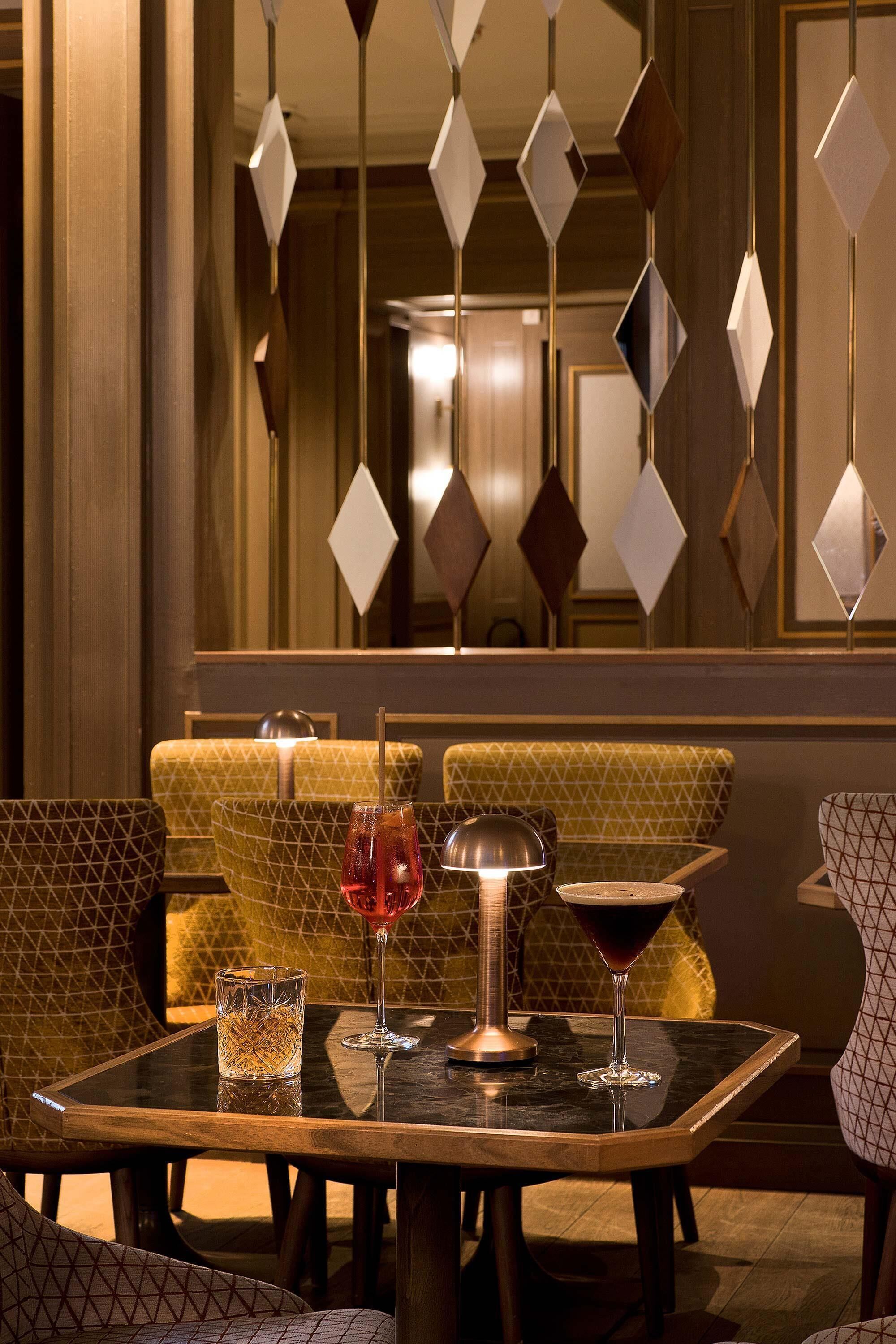 A restaurant interior with patterned seating, a table with drinks, and a decorative light fixture.
