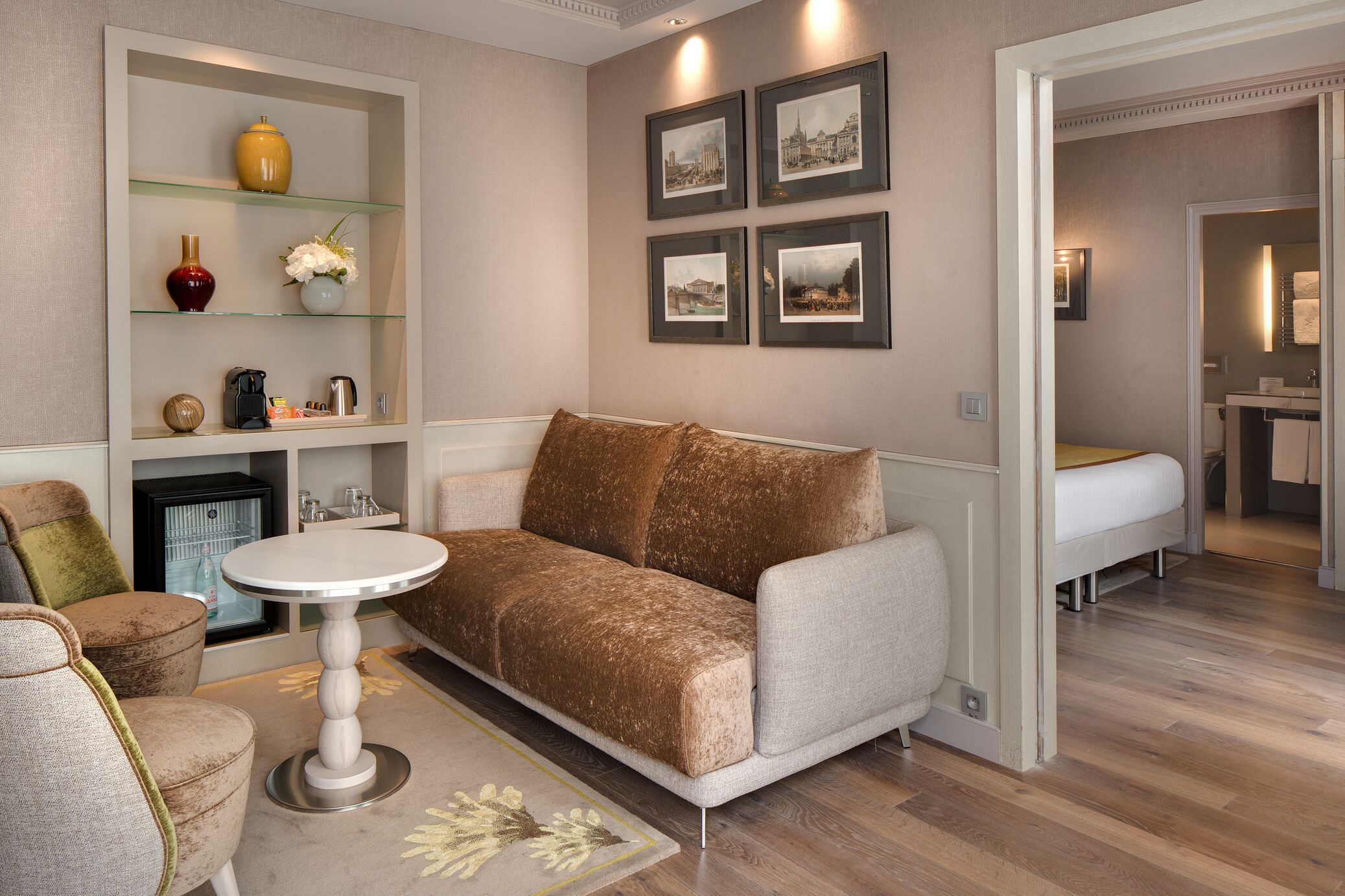 A living room with a sofa, a coffee table, and a fireplace. There are framed pictures on the wall and a shelf with decorative items.