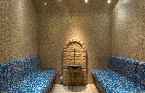 Una habitación con suelo de baldosas, un elemento central de piedra y dos bancos con cojines estampados.
