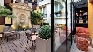 A modern outdoor patio with seating, a fountain, and a glass enclosure with a bookshelf. - Hotel Rochester Champs Elysées (Paris)