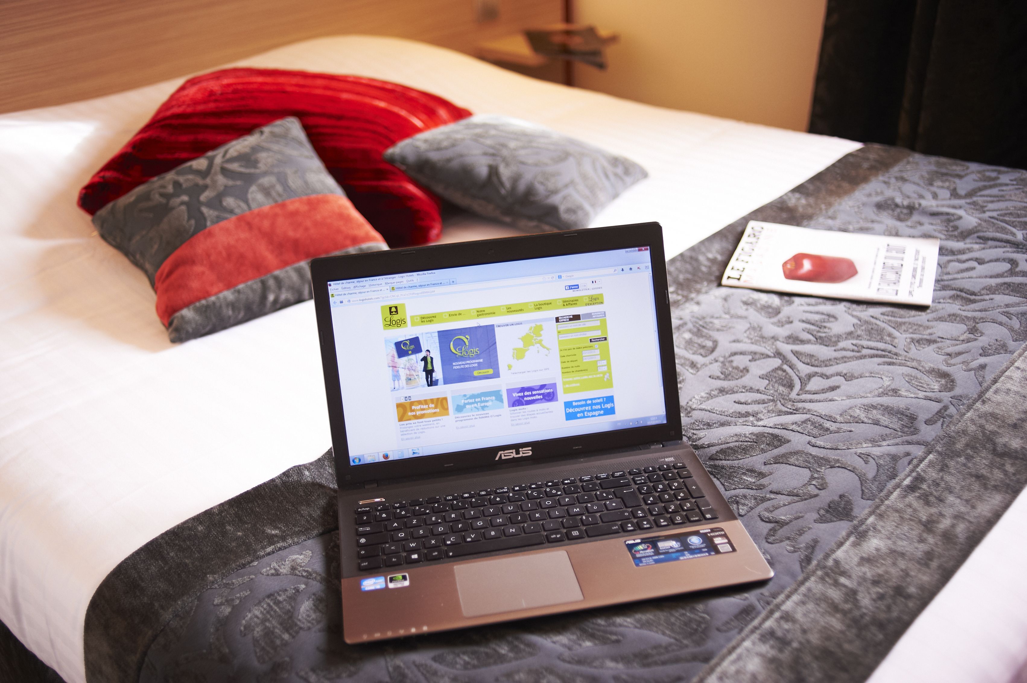Een laptop op een bed met een beddengoed met dessin, kussens en een klein kaartje.