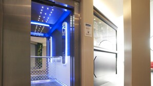 Un ascensor con techo iluminado en azul y puerta de vidrio.