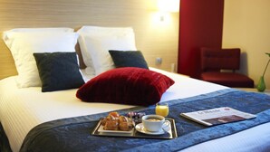 Habitación de hotel con una cama bien hecha, una bandeja con croissants y café, y un menú sobre la cama.