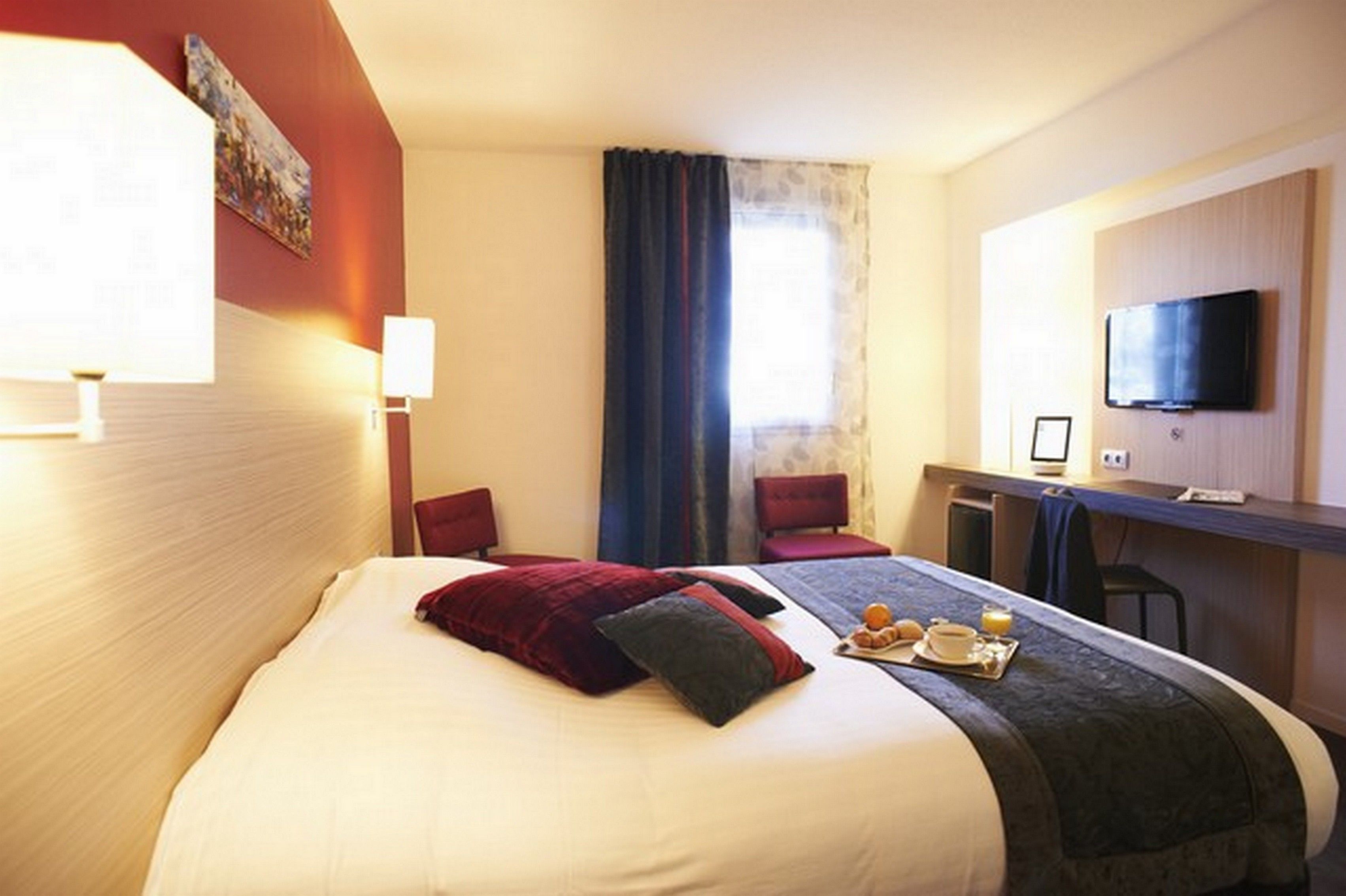 A hotel room with a bed, a desk, a television, and a window with curtains.