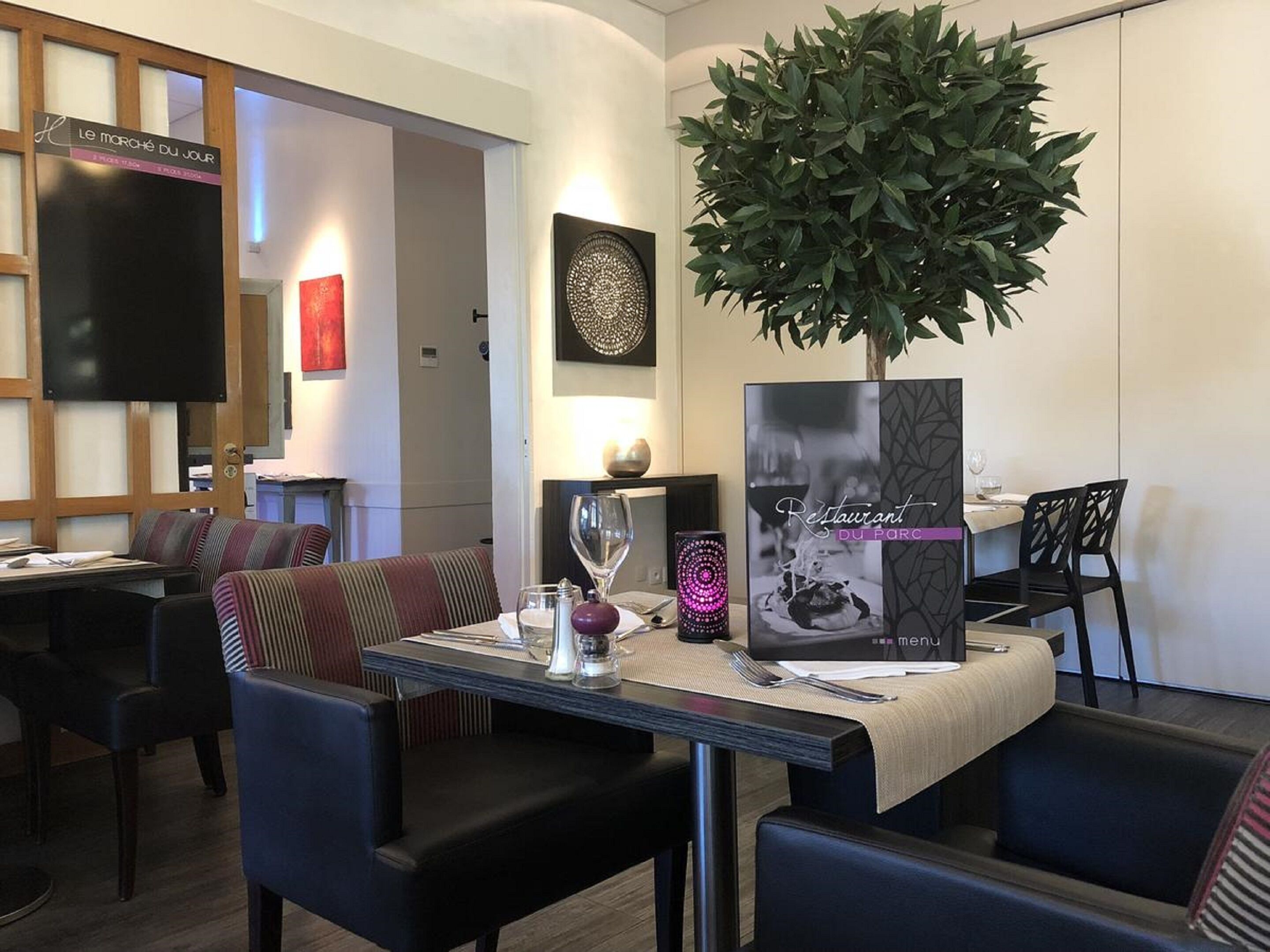 En restauranginteriör med ett bord dukat för två personer, en stor krukväxt och ett menyställ.