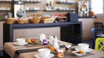 A breakfast setup with a table set for two, a coffee machine, and a variety of pastries and fruits on display in the background.