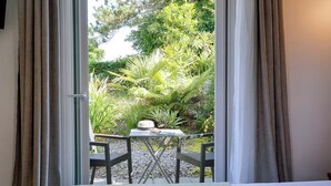 A room with a bed, a table with chairs, and a view of a garden through a window with curtains. - Brit Hotel Le Branhoc (Auray)
