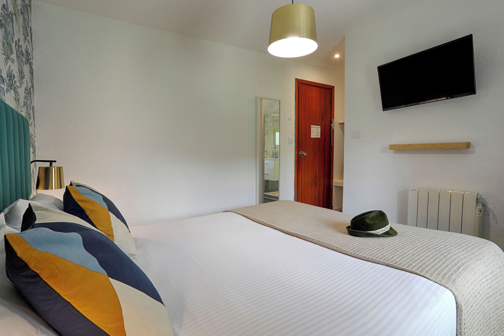 Ein Hotelzimmer mit Bett, Wandfernseher, Holztür und Heizkörper.