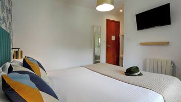 Una habitación de hotel con una cama, televisión montada en la pared, una puerta de madera y un radiador.