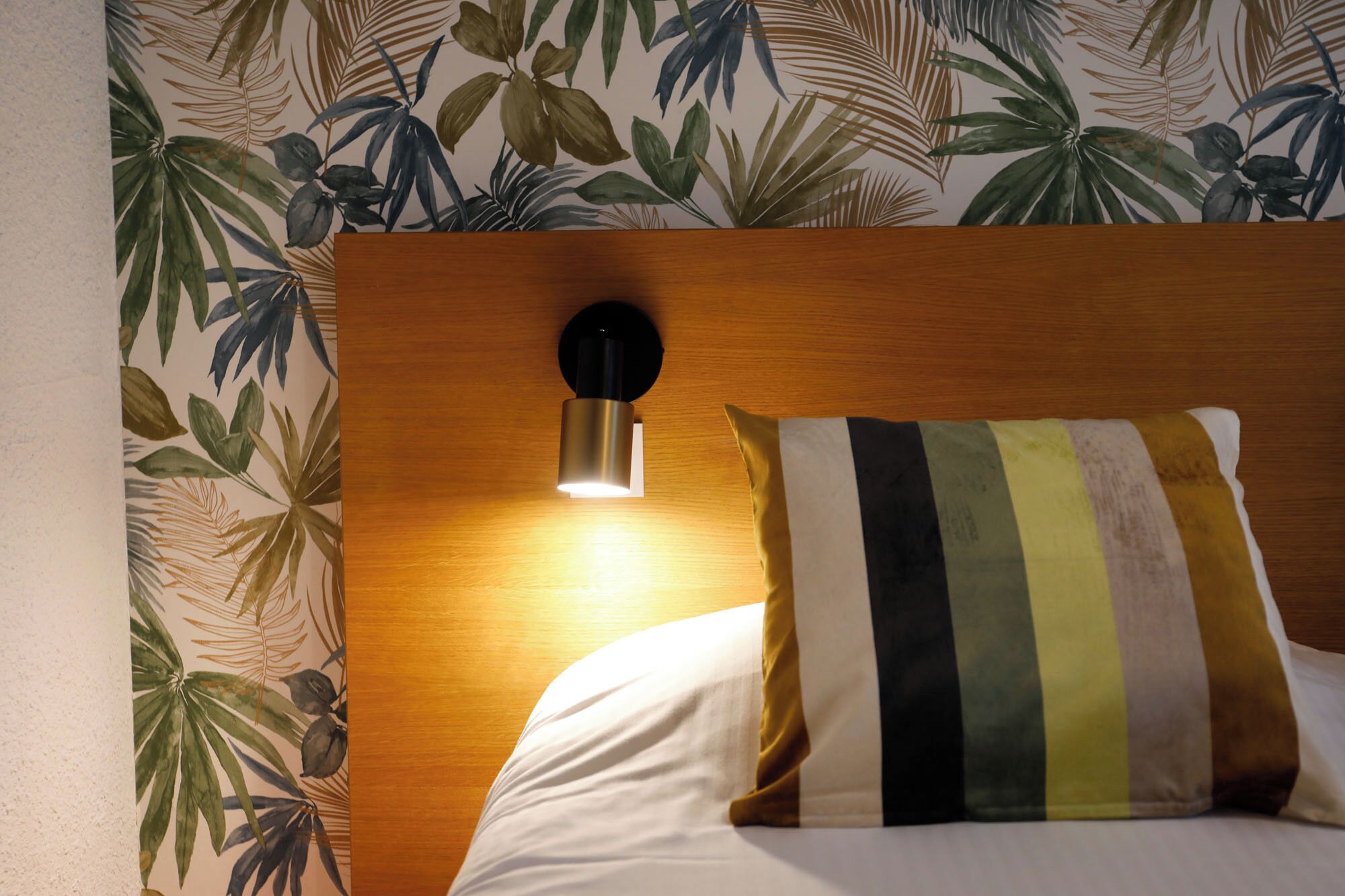 Una camera d'hotel con una testiera in legno, una lampada a parete e un cuscino a righe.