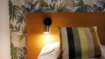 Una camera d'hotel con una testiera in legno, una lampada a parete e un cuscino a righe.