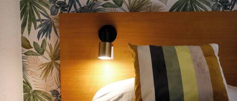 Quarto de hotel com cabeceira de madeira, luminária fixada na parede e almofada listrada.