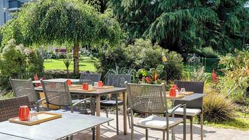 An outdoor patio with tables and chairs, surrounded by lush greenery and trees.