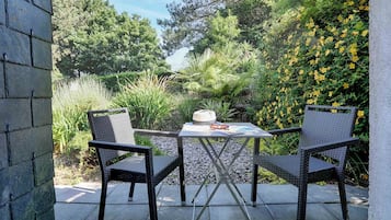 An outdoor patio with a table and two chairs, surrounded by lush greenery and yellow flowers.