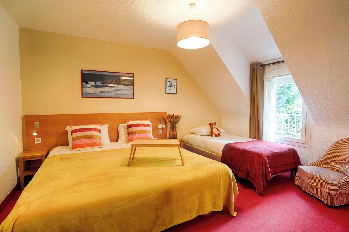 A hotel room with two beds, a wooden headboard, a painting, a window with curtains, and a red carpet.