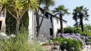 A modern house with a brick facade, surrounded by lush greenery and flowering plants. - Brit Hotel Le Branhoc (Auray)