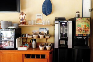 Una estación de café con una máquina de café, un refrigerador y una exhibición de granos de café y productos de pastelería.