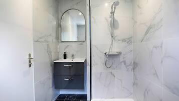 Un baño moderno con baldosas de mármol, ducha, lavabo con espejo y suelo de mármol oscuro.