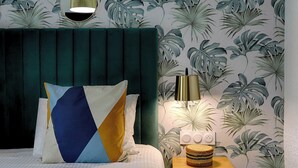 A bedroom with a green headboard, a geometric pillow, a bedside lamp, and a small wooden nightstand with a woven basket. - Brit Hotel Le Branhoc (Auray)