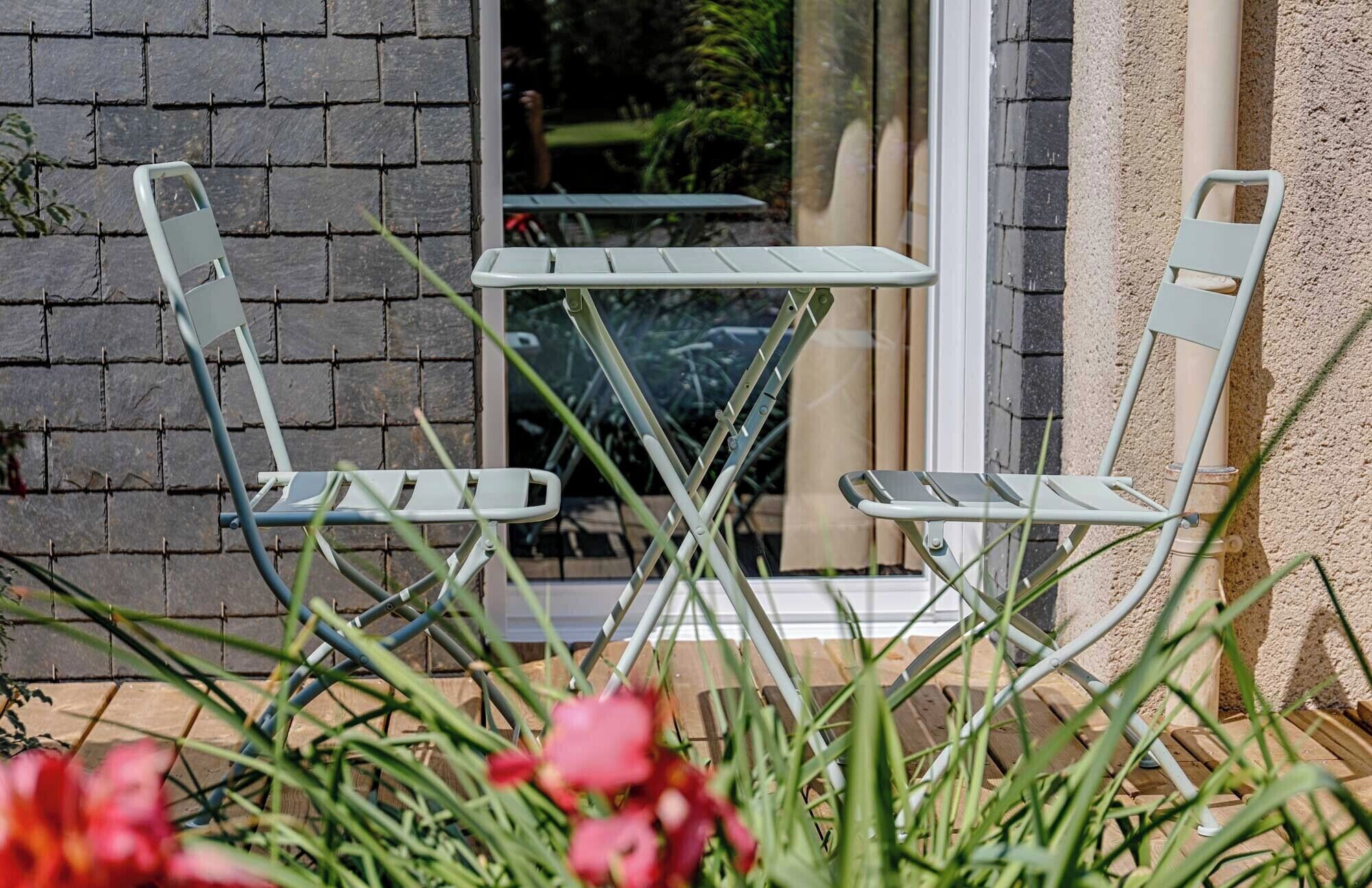 Two outdoor metal chairs and a small table in front of a window with a brick wall.