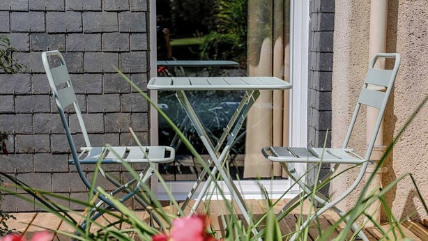 Two outdoor metal chairs and a small table in front of a window with a brick wall. - Brit Hotel Le Branhoc (Auray)