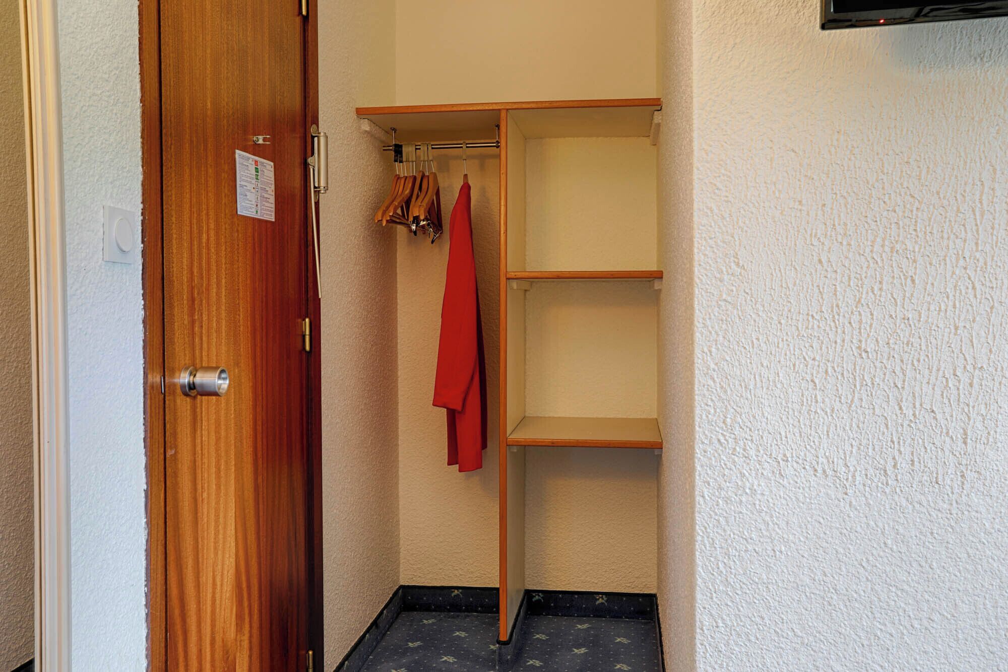 Une porte en bois avec une petite pancarte, un placard rempli de vêtements et une étagère.