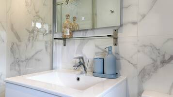 A bathroom with a large white sink, a mirror above it, and a glass shelf with decorative items.