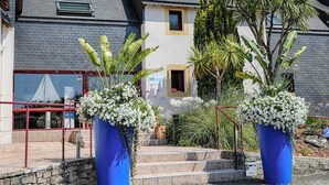 A hotel with a grey roof, a yellow facade, and a sign that reads "BRIT HOTEL". There are two large blue planters with white flowers in front of the entrance. - Brit Hotel Le Branhoc (Auray)