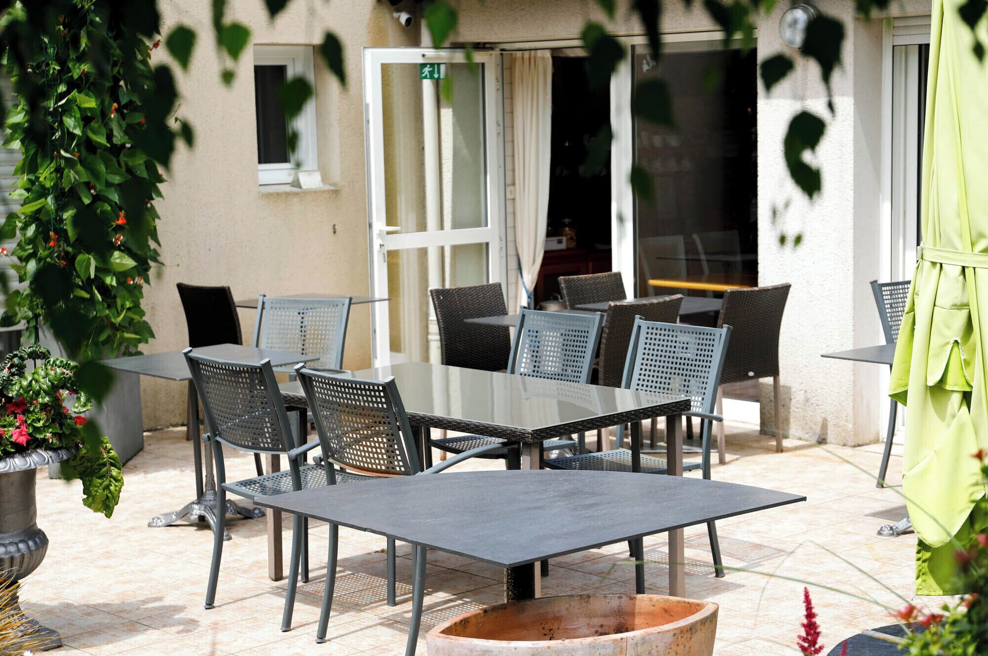 En udendørs terrasse med et bord, stole, en plantekasse og en dør til indgangen.