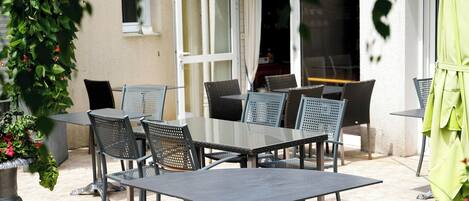 En udendørs terrasse med et bord, stole, en plantekasse og en dør til indgangen.