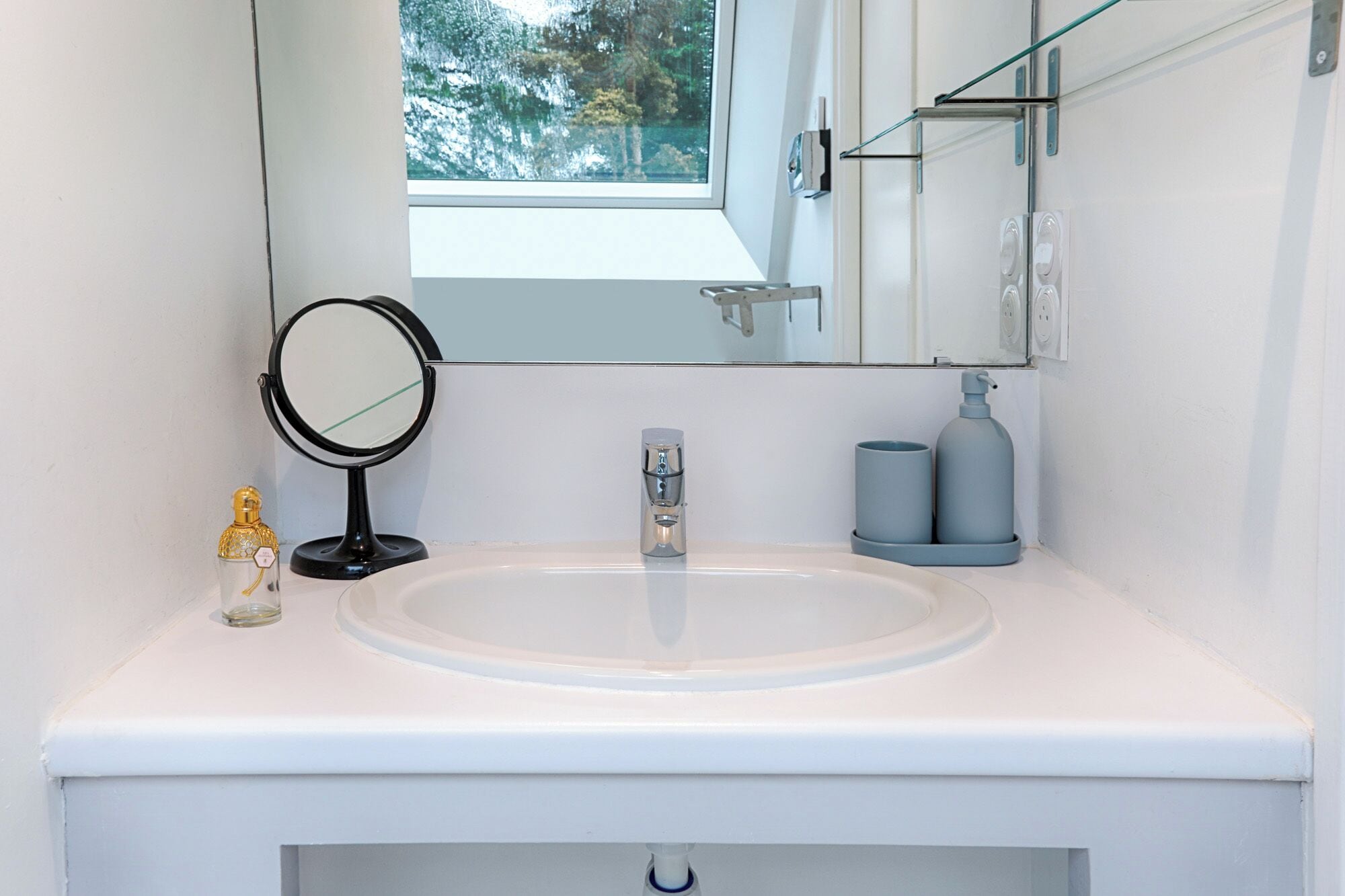 A bathroom with a white sink, a round mirror, a faucet, and a window above the mirror.