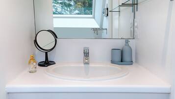 A bathroom with a white sink, a round mirror, a faucet, and a window above the mirror.