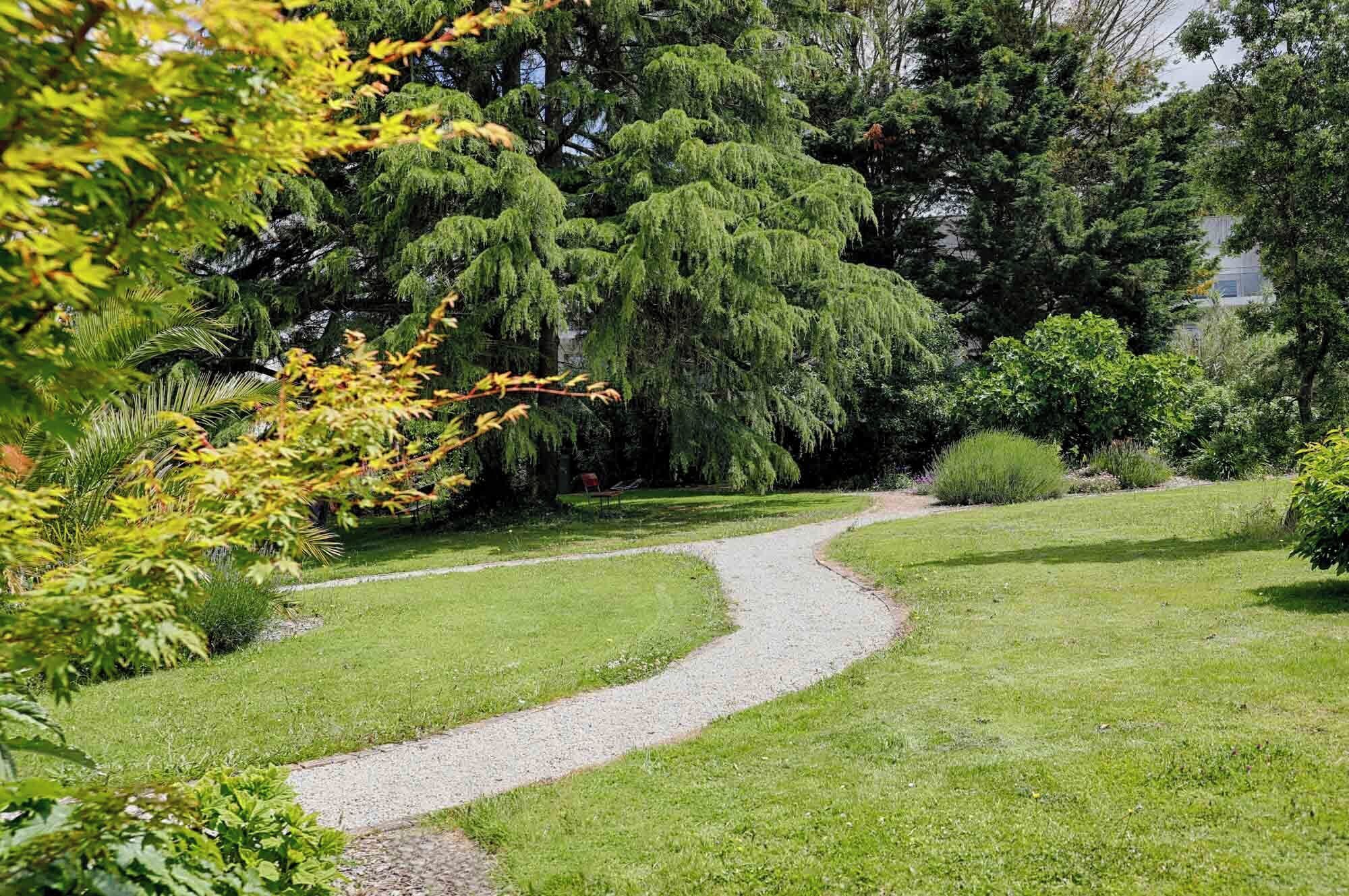 Un sendero de grava serpentea por un jardín bien cuidado, con varios árboles y arbustos.