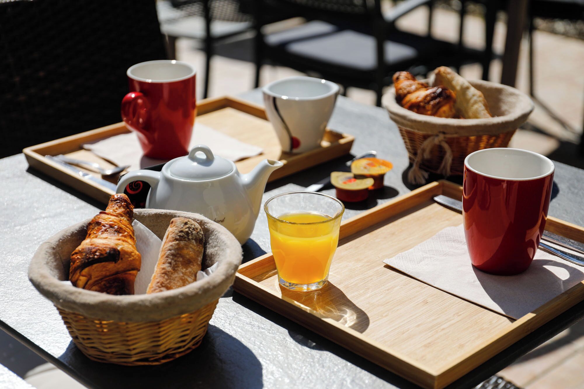 A breakfast tray with bread, a teapot, cups, and a glass of orange juice.