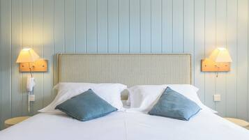 A neatly made bed with two pillows, a headboard, and two wall-mounted lamps on either side.