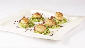 A white rectangular plate with seared scallops on a bed of lettuce, garnished with a dark sauce.